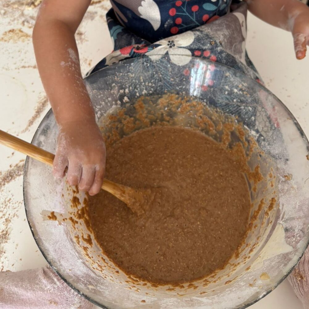 Toddler-sized hands mixing batter in a glass bowl